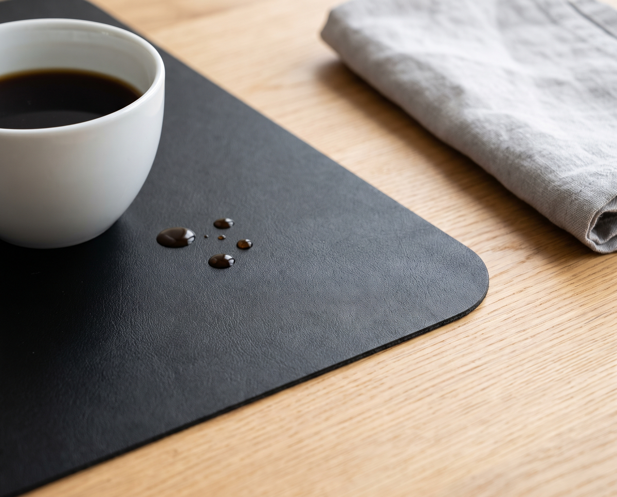 Gouttes de café qui perlent sur le sous-main noir à côté d’une tasse