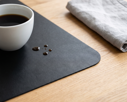Gouttes de café qui perlent sur le sous-main noir à côté d’une tasse