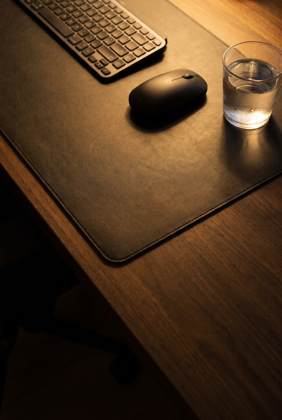 Sous-main noir le soir, avec une souris, un clavier et un verre d’eau